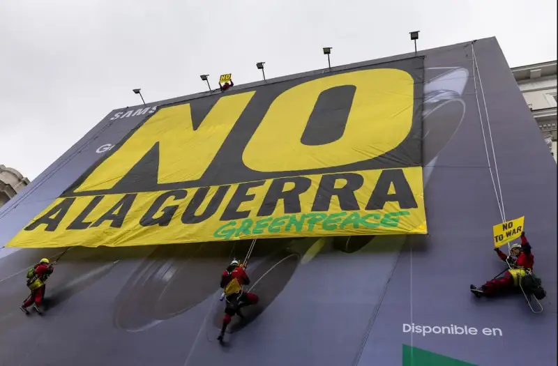 Activistas pacifistas y ambientalistas despliegan, sobre un gran aviso comercial, una pancarta en rechazo a la guerra contra Irán, el pasado marzo en Madrid. Además del costo en vidas y en personas heridas y desplazadas, el conflicto que ya lleva seis meses causa enormes daños materiales, impactos negativos en la economía global, incremento del gasto militar y daños ambientales. Imagen: Greenpeace